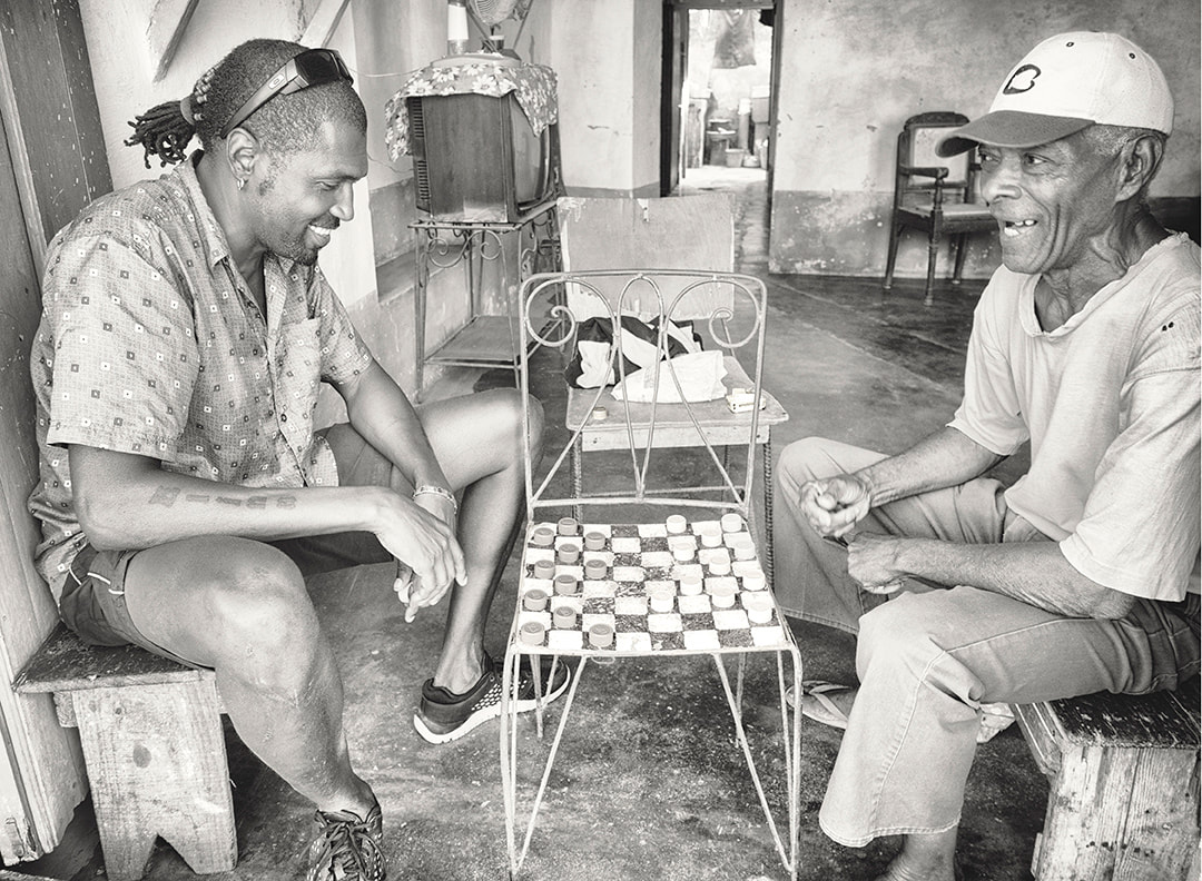 two men playing checkers with bottle tops in window.  Trinidad, cuba. black and white.